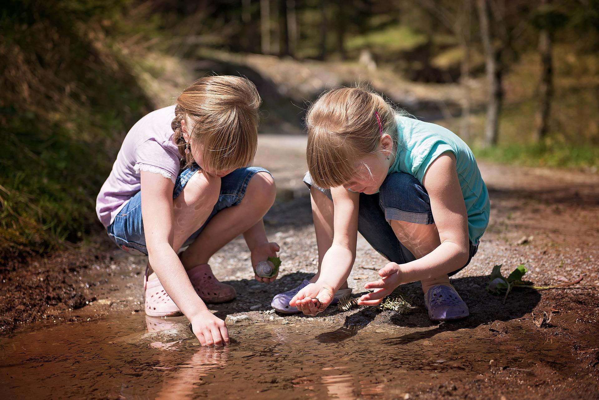2 tüdrukut kükitavad lombi juures ja uurivad tigusid ja kivikesi. Väikeste teadlaste klubi